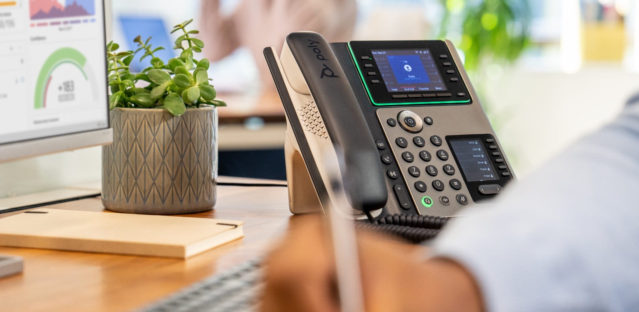 Man at office desk, writing notes while using Poly Edge E450 IP desk phone 